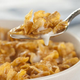 Cereal bowl of cornflakes and milk with spoon lifting a bite from the bowl
